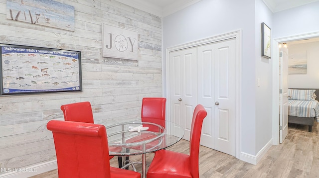 dining space with light hardwood / wood-style floors, crown molding, and wood walls