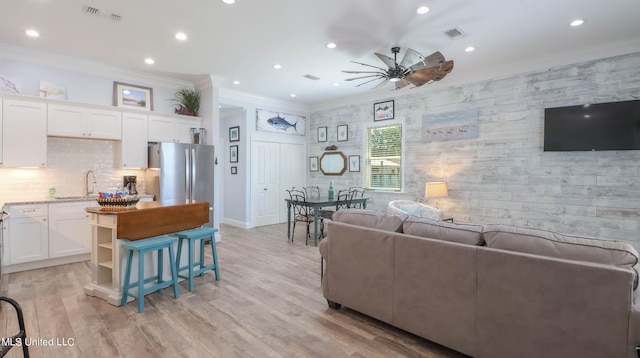 living room with light hardwood / wood-style flooring, crown molding, sink, and ceiling fan