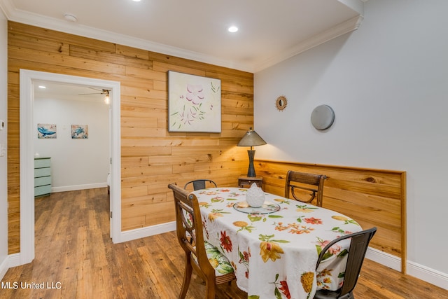 dining room with crown molding, hardwood / wood-style floors, wooden walls, and ceiling fan