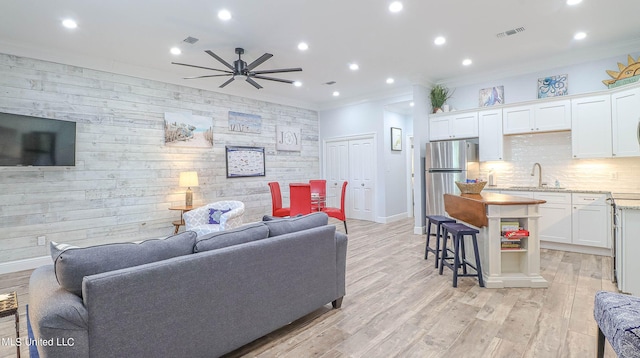 living room with crown molding, sink, light wood-type flooring, and ceiling fan