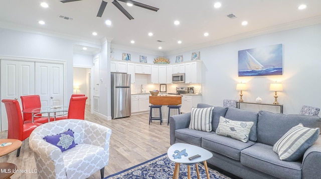 living room featuring ornamental molding, sink, light hardwood / wood-style flooring, and ceiling fan