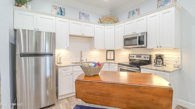 kitchen featuring light hardwood / wood-style floors, stainless steel appliances, white cabinets, light stone counters, and ornamental molding