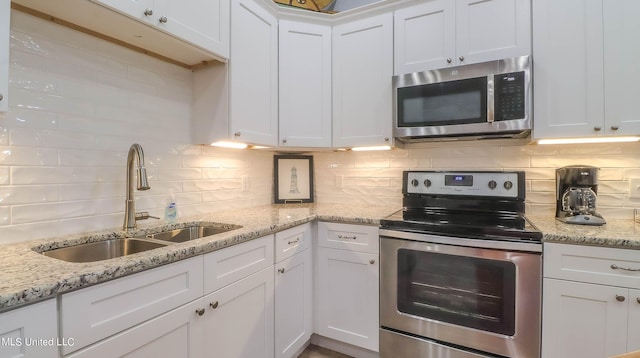 kitchen featuring white cabinets, tasteful backsplash, appliances with stainless steel finishes, light stone countertops, and sink