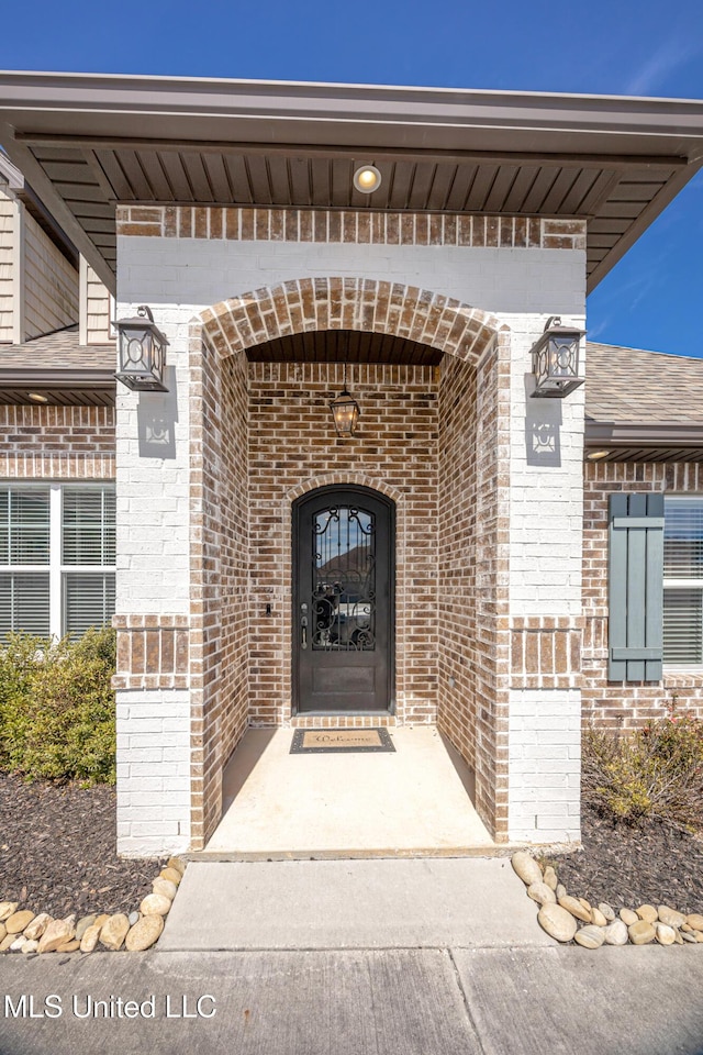 view of exterior entry featuring roof with shingles and brick siding