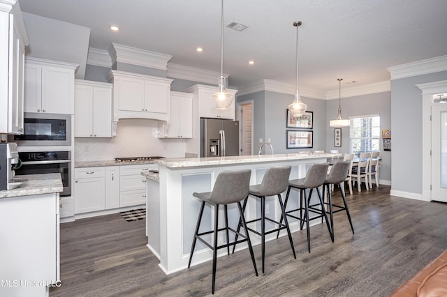 kitchen with visible vents, appliances with stainless steel finishes, dark wood-type flooring, white cabinets, and an island with sink