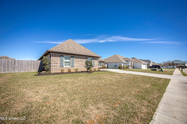 view of front of home with driveway, roof with shingles, fence, a front lawn, and brick siding