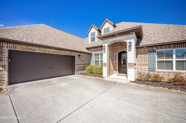 view of front of home with concrete driveway, brick siding, roof with shingles, and an attached garage