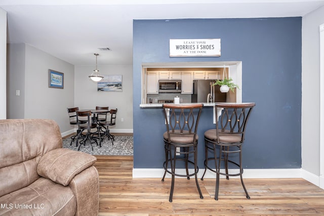 kitchen featuring a breakfast bar area, pendant lighting, light wood-type flooring, and appliances with stainless steel finishes