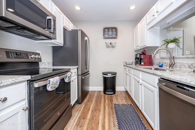 kitchen with light stone countertops, stainless steel appliances, sink, light hardwood / wood-style flooring, and white cabinetry