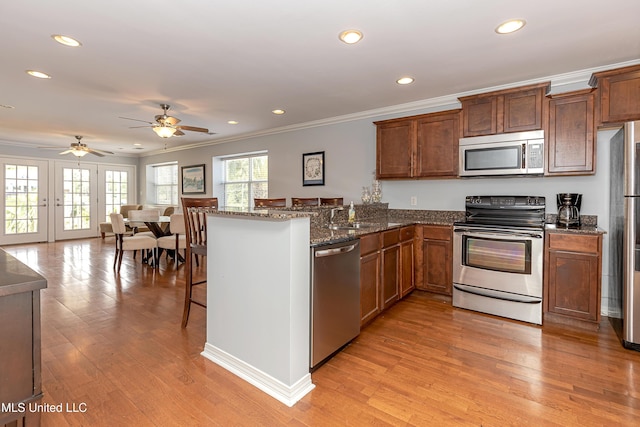 kitchen featuring ceiling fan, appliances with stainless steel finishes, a healthy amount of sunlight, a kitchen bar, and kitchen peninsula