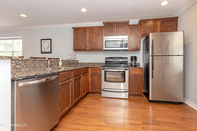 kitchen featuring sink, crown molding, dark stone countertops, light wood-type flooring, and stainless steel appliances