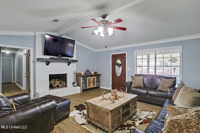 living room featuring hardwood / wood-style flooring, ceiling fan, ornamental molding, lofted ceiling with beams, and a brick fireplace