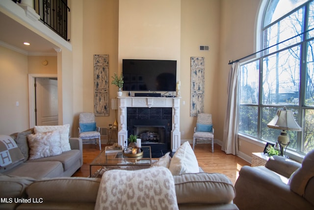 living room with a tiled fireplace, crown molding, wood-type flooring, and a high ceiling