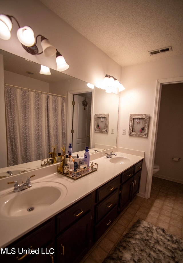 bathroom featuring tile patterned flooring, vanity, toilet, and a textured ceiling