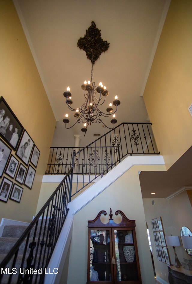 stairway featuring a towering ceiling, an inviting chandelier, and crown molding