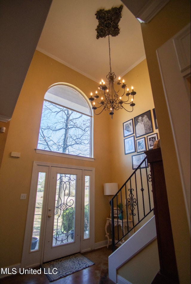 entrance foyer with ornamental molding, a towering ceiling, and an inviting chandelier