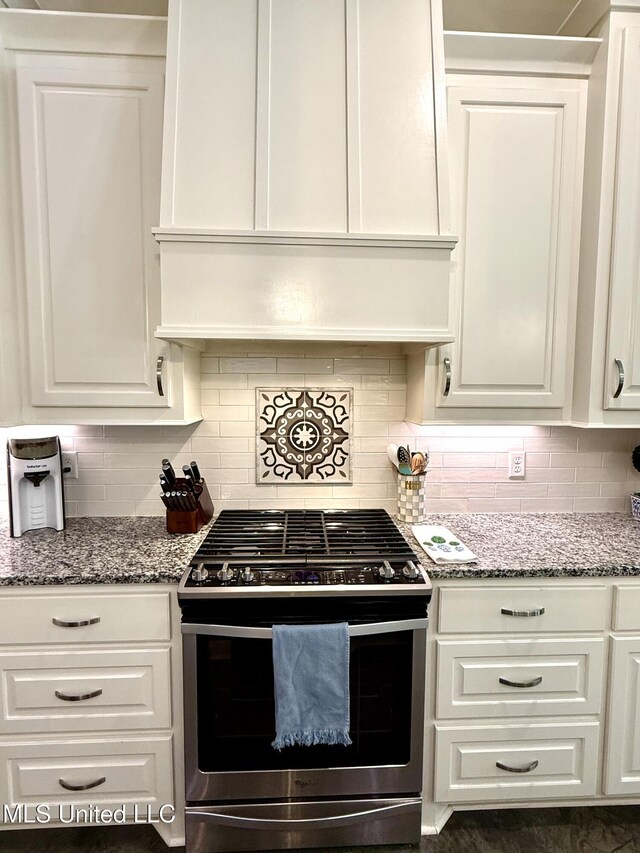 kitchen featuring stainless steel gas range oven, wall chimney range hood, white cabinets, and backsplash