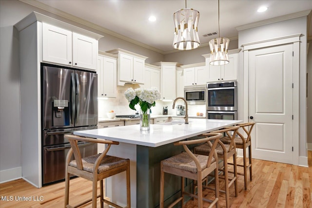 kitchen with white cabinets, appliances with stainless steel finishes, decorative light fixtures, sink, and a breakfast bar area