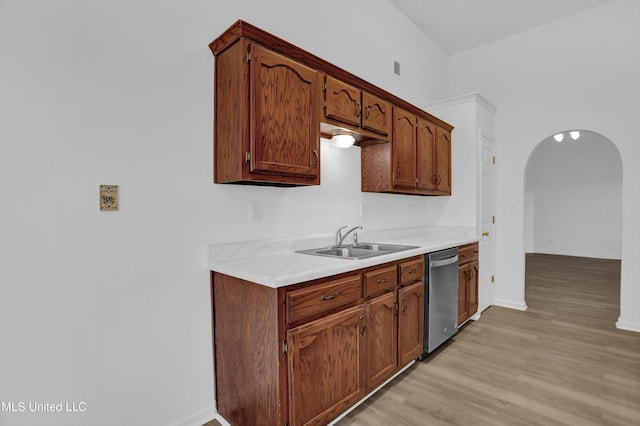 kitchen featuring arched walkways, a sink, light countertops, dishwasher, and light wood finished floors