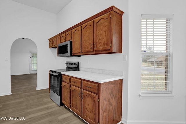 kitchen featuring arched walkways, range with electric stovetop, a wealth of natural light, light countertops, and stainless steel microwave