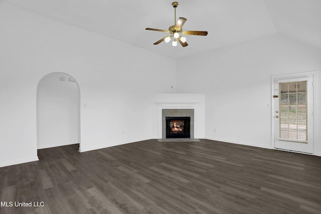 unfurnished living room with arched walkways, dark wood finished floors, a ceiling fan, a tiled fireplace, and lofted ceiling