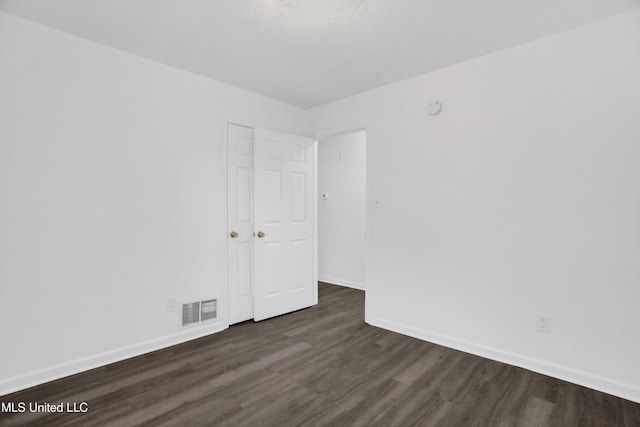 unfurnished room featuring dark wood-style flooring, visible vents, a textured ceiling, and baseboards