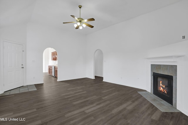 unfurnished living room with arched walkways, dark wood finished floors, and a tile fireplace