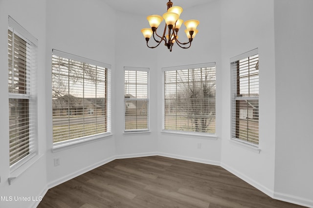 unfurnished dining area featuring a chandelier, a high ceiling, baseboards, and wood finished floors