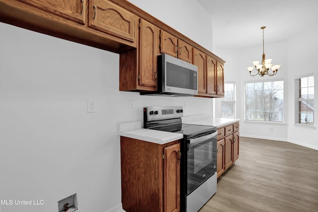 kitchen featuring light wood-style flooring, a notable chandelier, light countertops, appliances with stainless steel finishes, and brown cabinetry