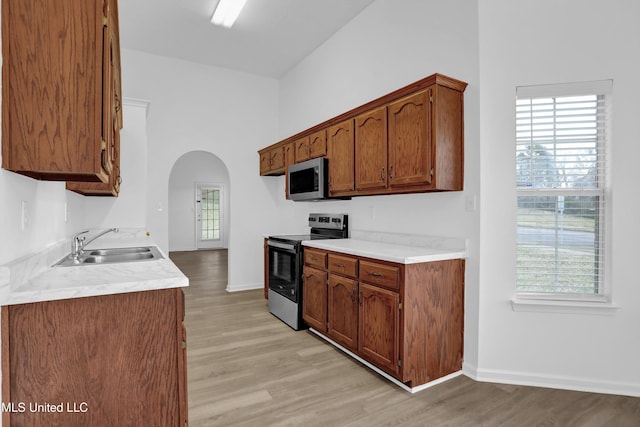 kitchen with arched walkways, appliances with stainless steel finishes, light countertops, light wood-type flooring, and a sink