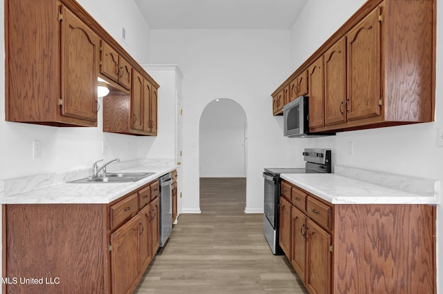 kitchen featuring arched walkways, appliances with stainless steel finishes, light countertops, light wood-style floors, and a sink