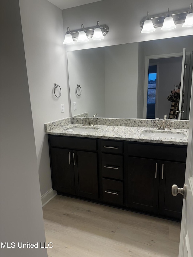 bathroom with double vanity, wood finished floors, a sink, and baseboards