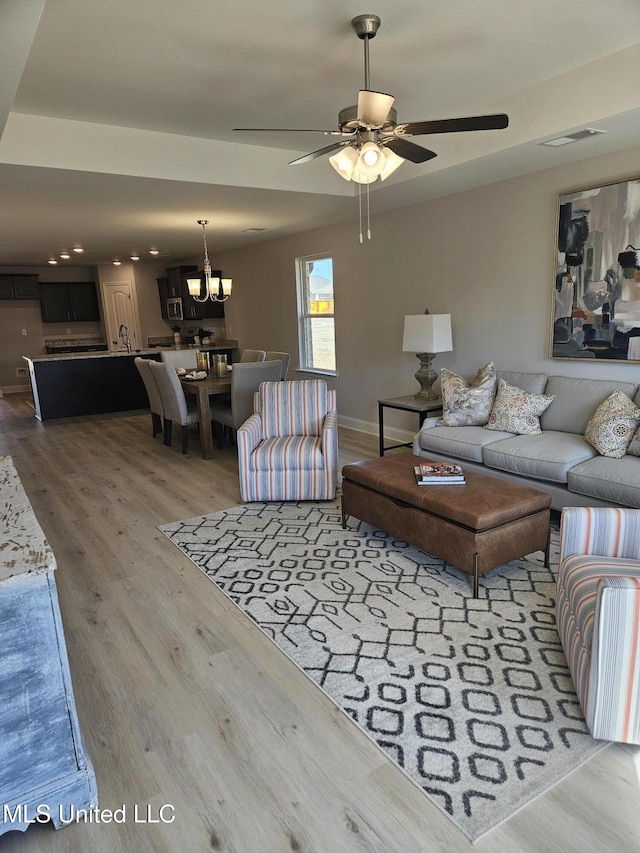 living room featuring visible vents, ceiling fan with notable chandelier, light wood-style flooring, and baseboards