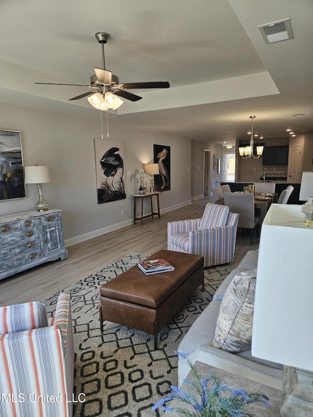 living area with baseboards, visible vents, wood finished floors, and ceiling fan with notable chandelier