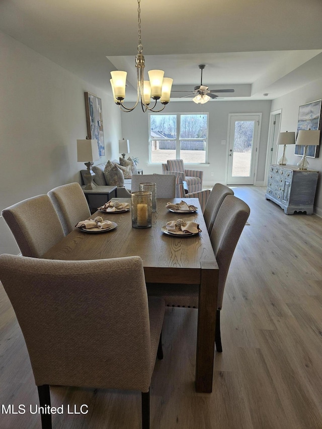 dining space featuring a raised ceiling, a notable chandelier, and wood finished floors