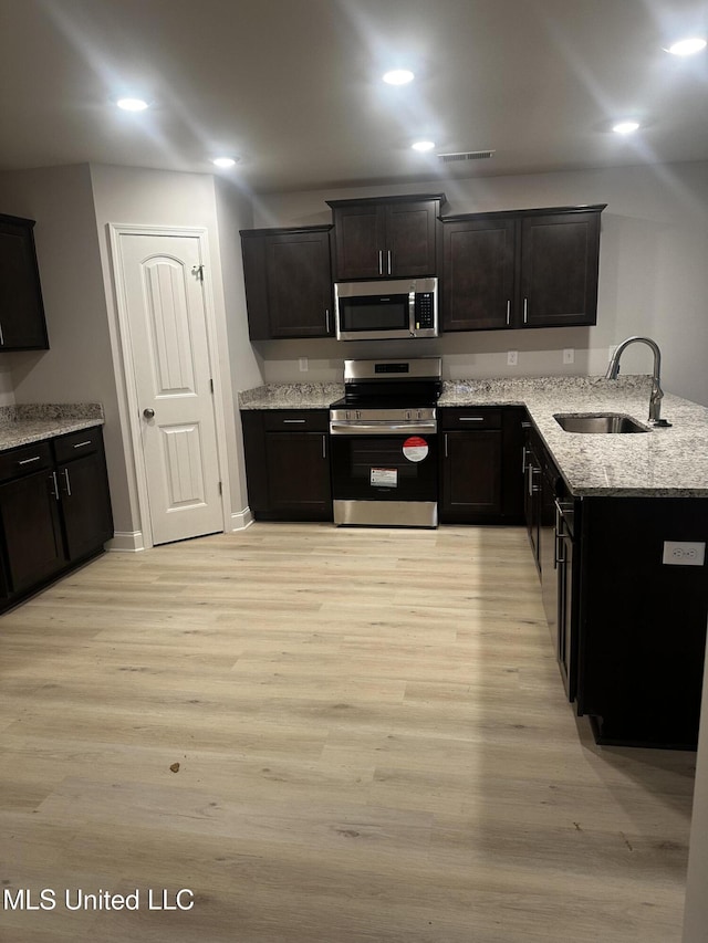 kitchen with appliances with stainless steel finishes, light wood-type flooring, a sink, and light stone counters