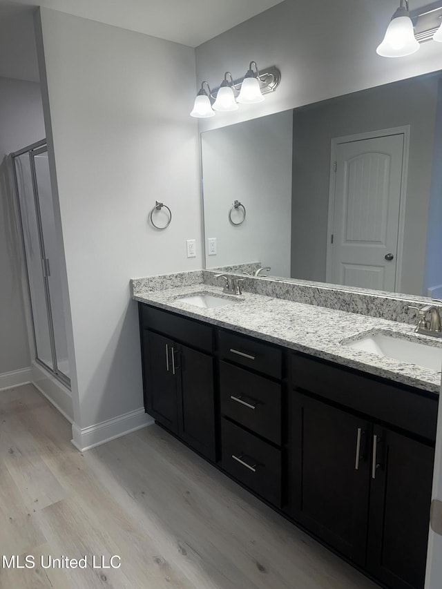 bathroom with a stall shower, double vanity, a sink, and wood finished floors