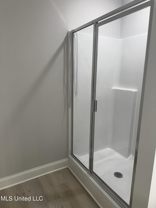 full bathroom featuring baseboards, wood finished floors, and a shower stall