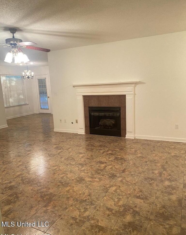 unfurnished living room featuring ceiling fan with notable chandelier, a textured ceiling, and a tile fireplace