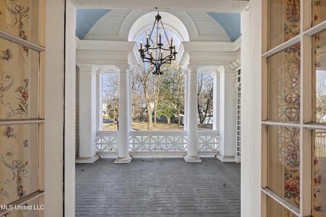 interior space featuring brick floor, a notable chandelier, a healthy amount of sunlight, vaulted ceiling, and ornate columns