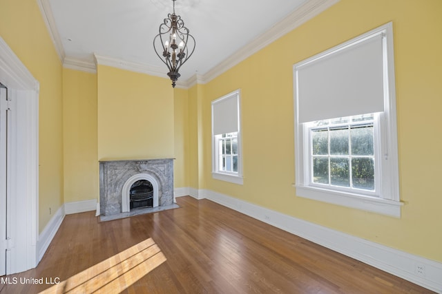 unfurnished living room with crown molding, a notable chandelier, a premium fireplace, wood finished floors, and baseboards