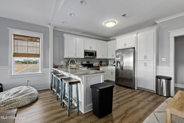 kitchen with a kitchen breakfast bar, dark wood-type flooring, stainless steel appliances, light stone countertops, and white cabinets