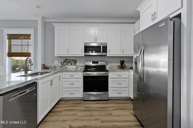 kitchen featuring white cabinets, appliances with stainless steel finishes, light stone countertops, hardwood / wood-style flooring, and sink