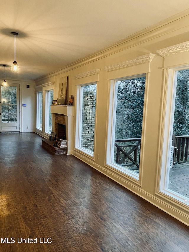 unfurnished living room with dark wood-style floors, a healthy amount of sunlight, a brick fireplace, and crown molding