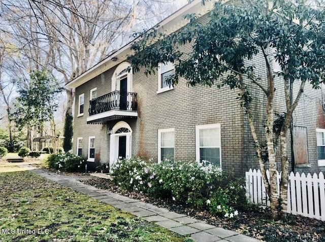 view of front of property with a balcony, fence, and brick siding