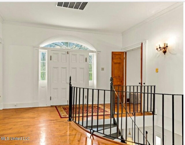 foyer entrance featuring baseboards, wood finished floors, visible vents, and crown molding