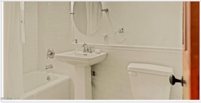 full bath featuring shower / bathtub combination, wainscoting, toilet, and tile walls