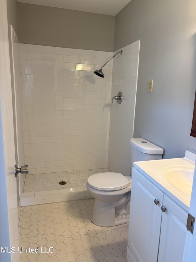 bathroom with tiled shower, tile patterned floors, vanity, and toilet