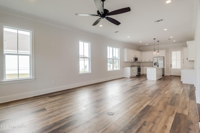 unfurnished living room with a healthy amount of sunlight, wood finished floors, and crown molding