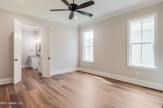 unfurnished bedroom with baseboards, crown molding, a sink, and light wood finished floors